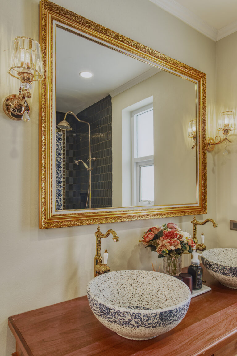 Detail of bathroom showing double vanity and large mirror with shower area in reflection