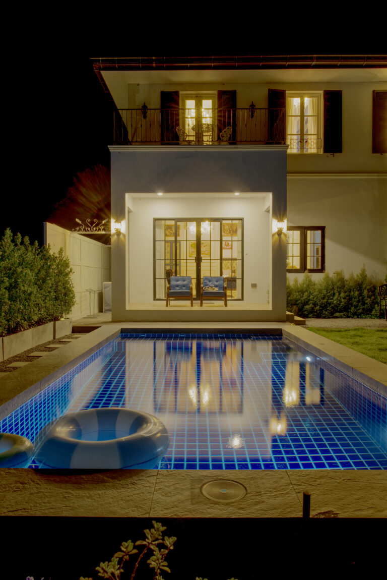 Swimming pool view at night with the house in background and sitting area