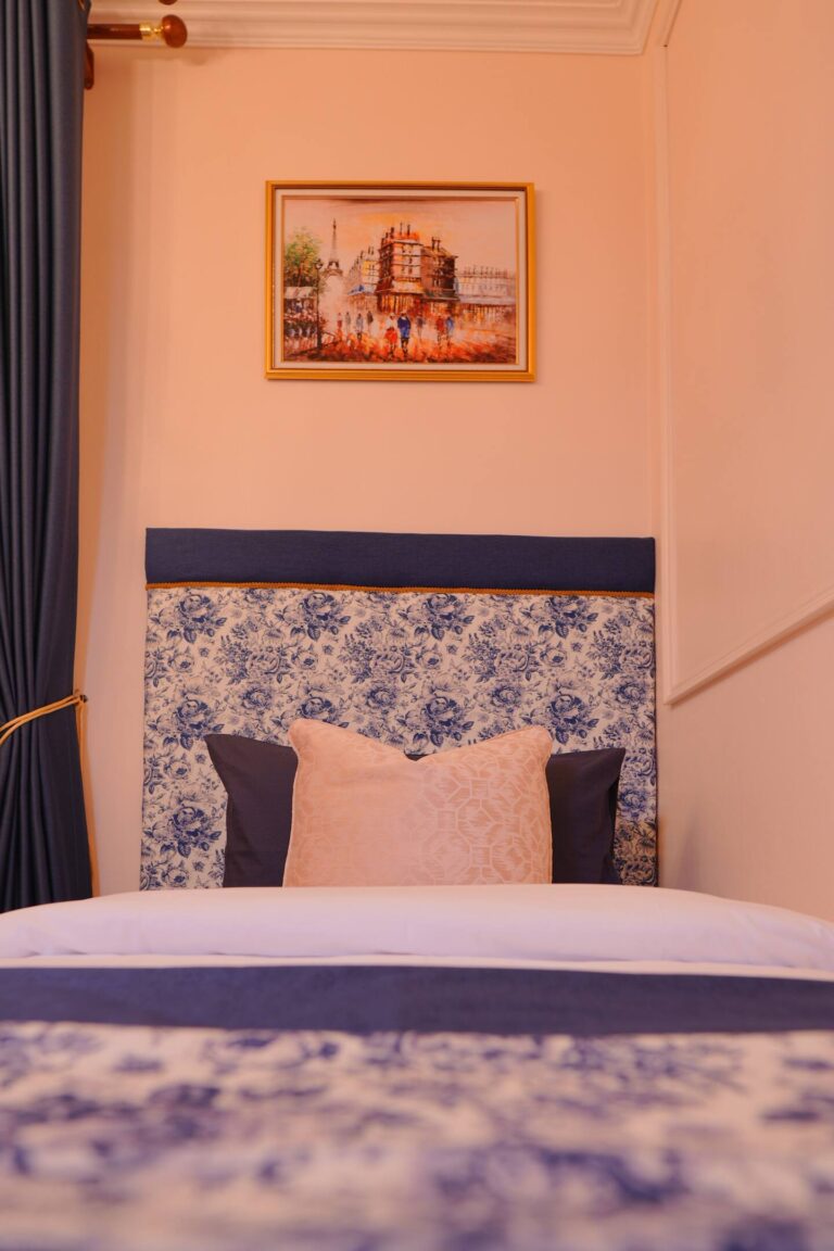 Bed detail with headboard using soft fabrics and painting of Paris